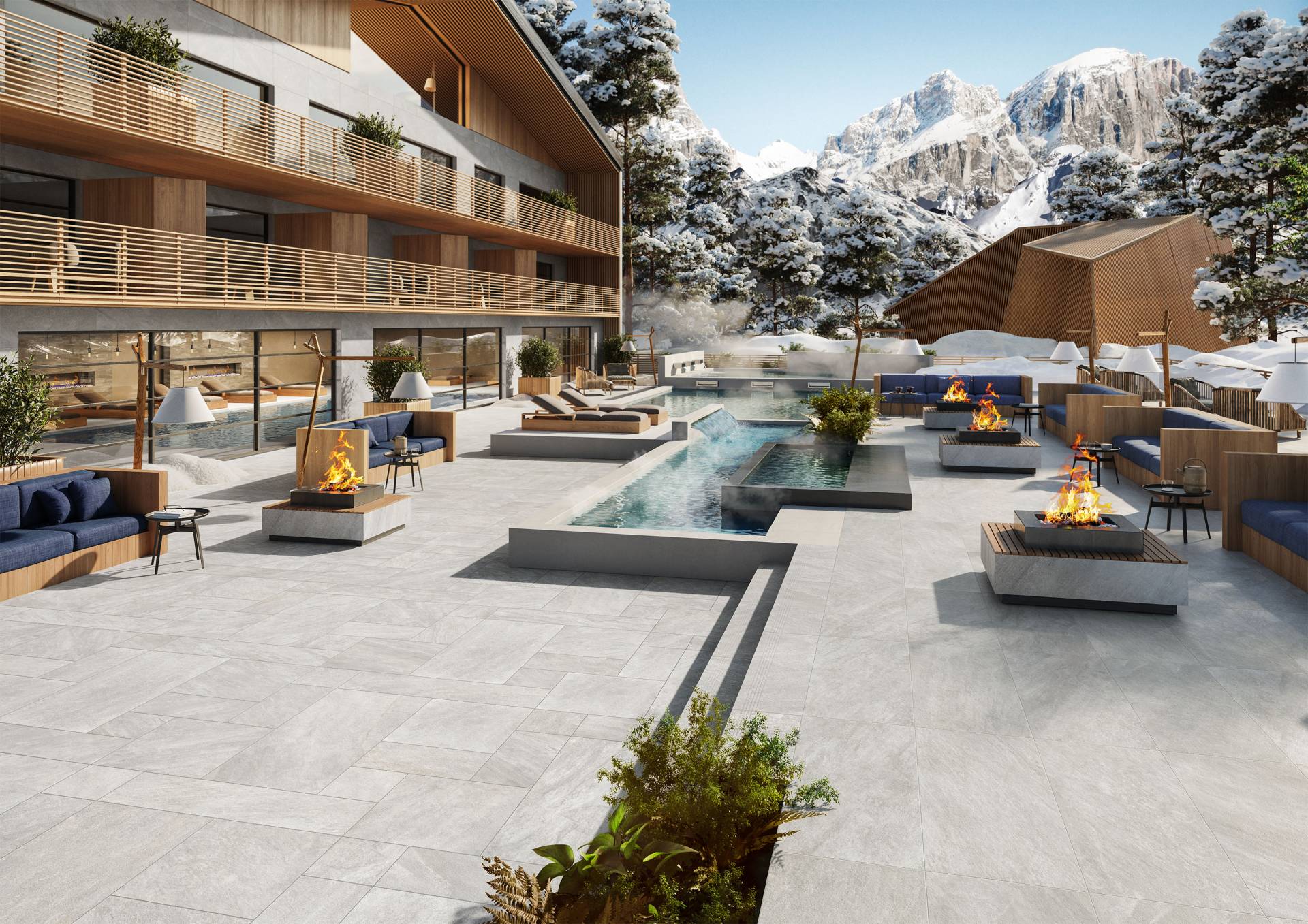 A luxurious outdoor patio at a mountain resort features a rectangular pool, modern fire pits, and comfortable seating. The backdrop includes snow-capped mountains and pine trees, with a contemporary building to the left.