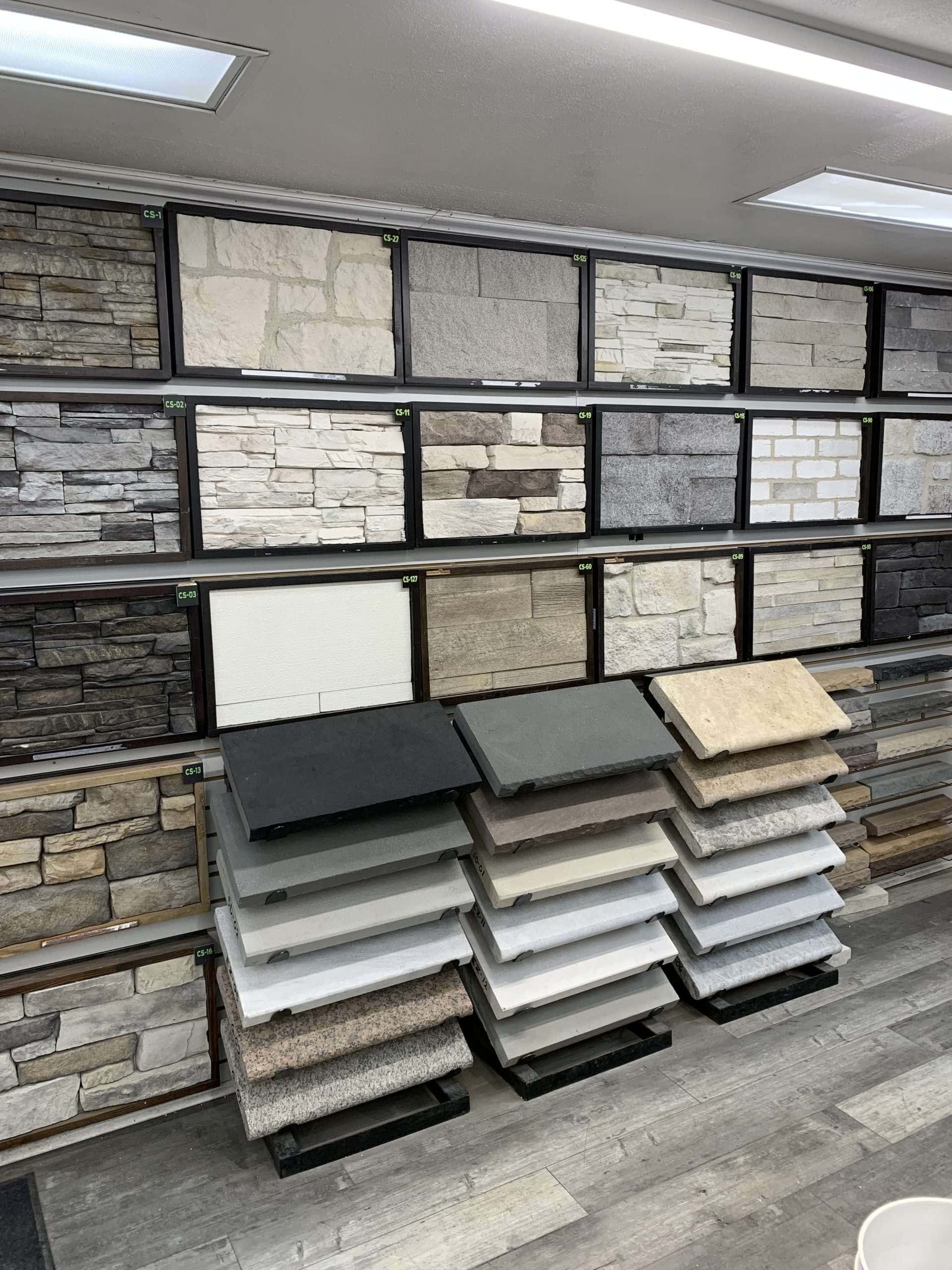Display of various stone and brick veneer samples mounted on a wall, with multiple stacks of sample tiles organized on stands below. The wall features different colors and textures, showcasing diverse design options.